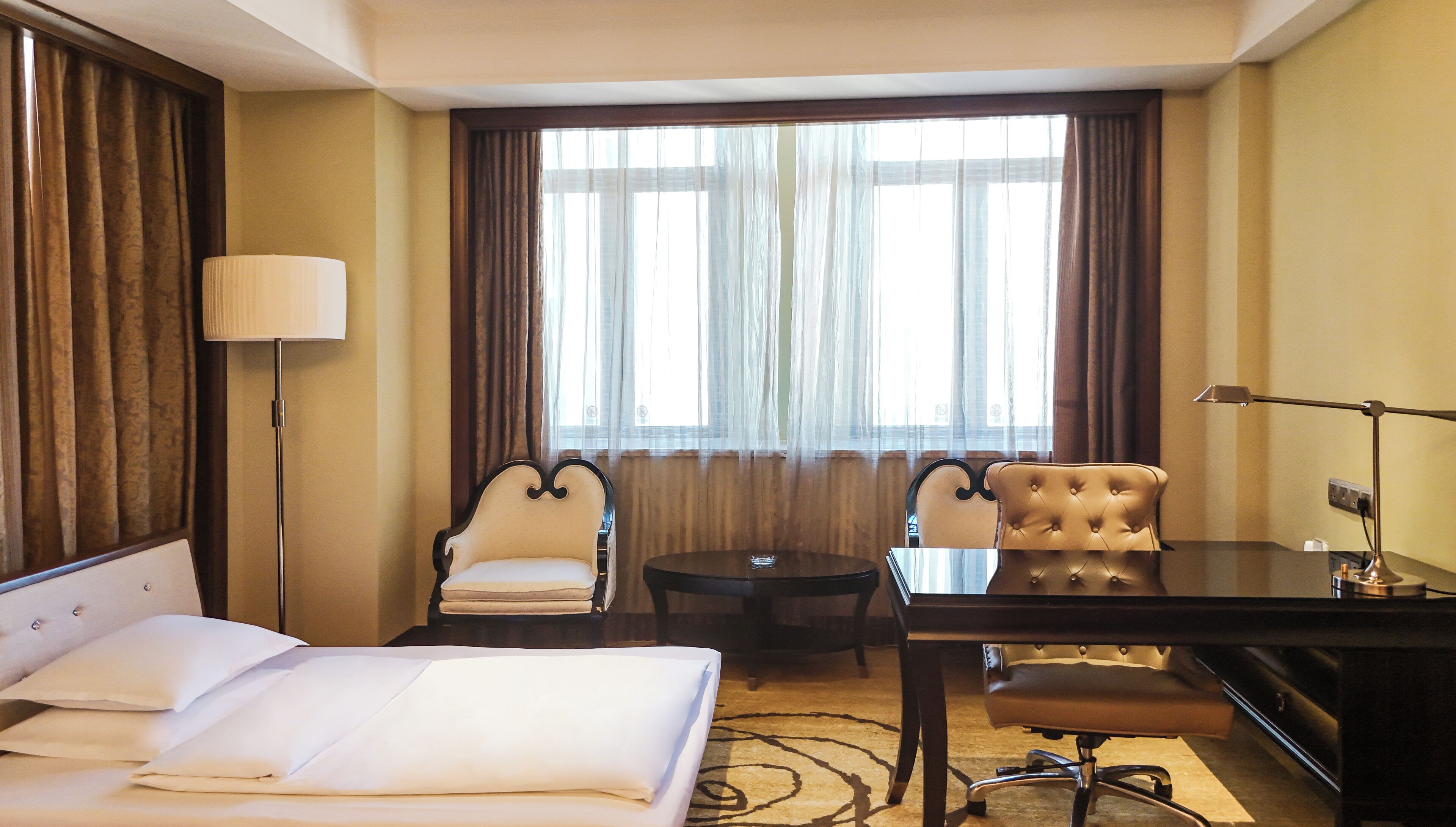 A hotel room with a bed, two armchairs, a desk, and a lamp.