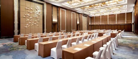 Un salón de conferencias con filas de mesas y sillas, alfombra estampada y luminarias de techo decoradas.