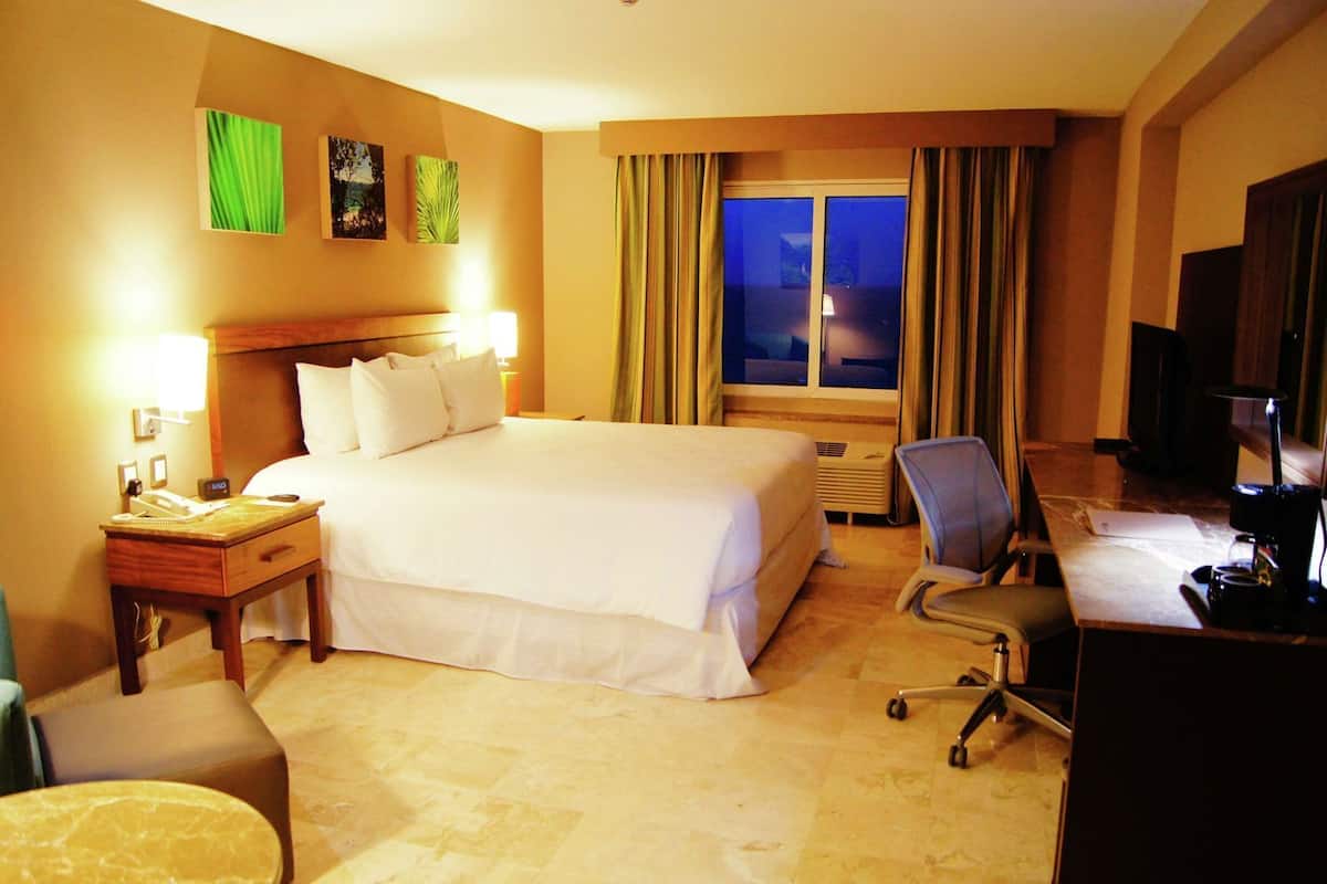 A hotel room with a bed, desk, chair, and a window with curtains.