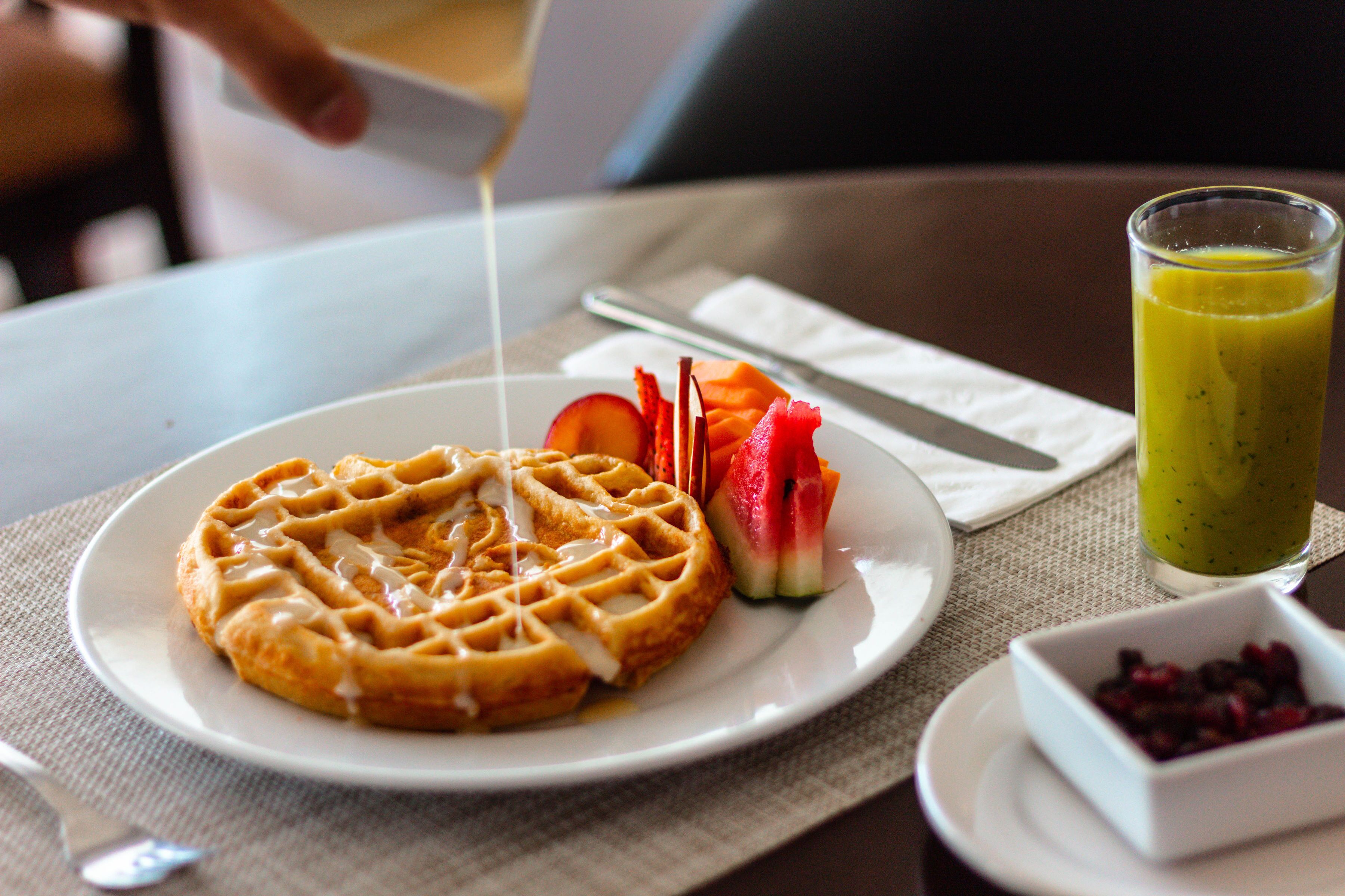 A plate with a waffle, sliced strawberries, and a glass of green smoothie on a table.