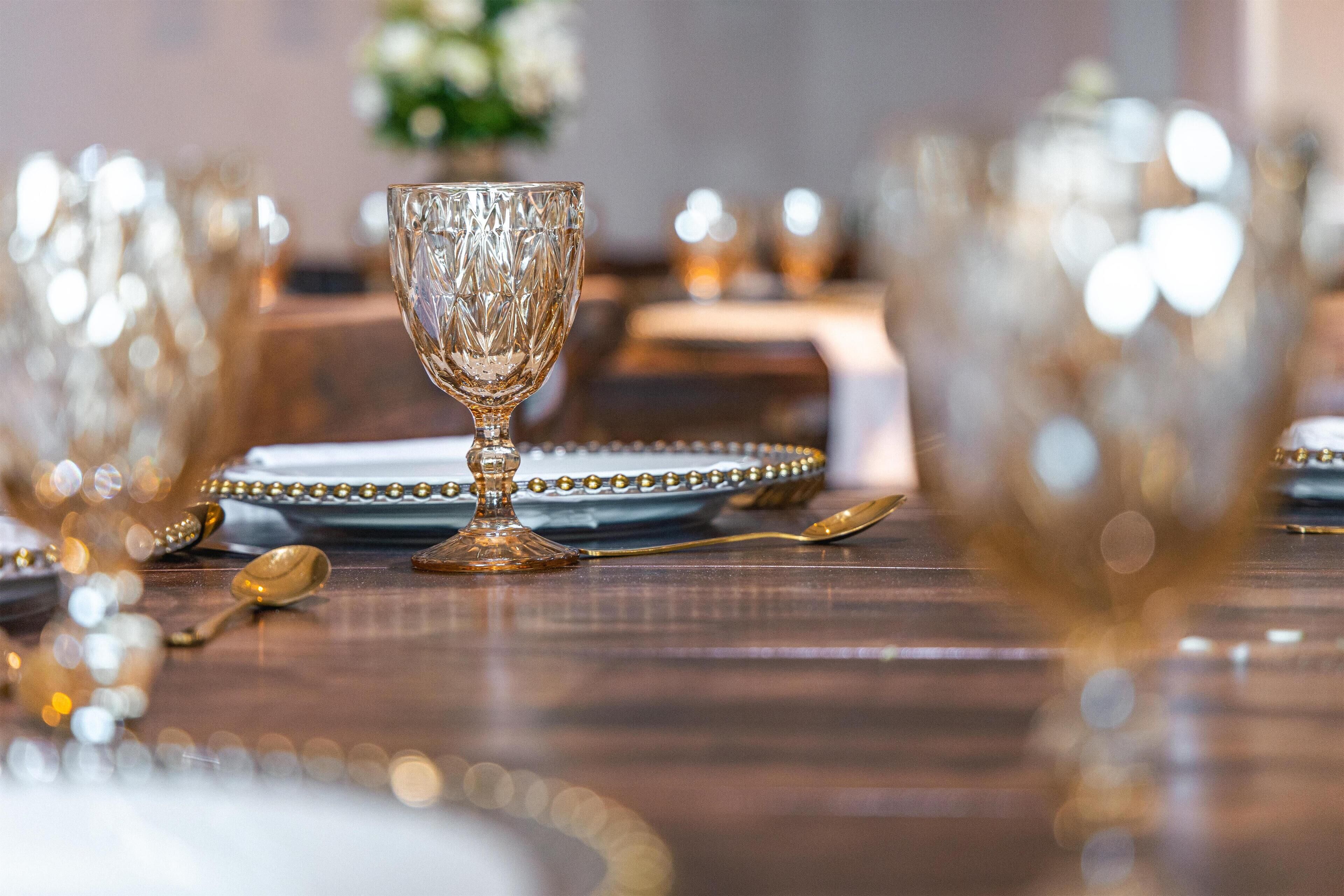 A dining table set with gold-rimmed glassware and plates, with a spoon and a gold-colored napkin holder.