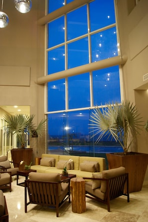 A spacious living area with a large window, a sofa, armchairs, and potted plants.