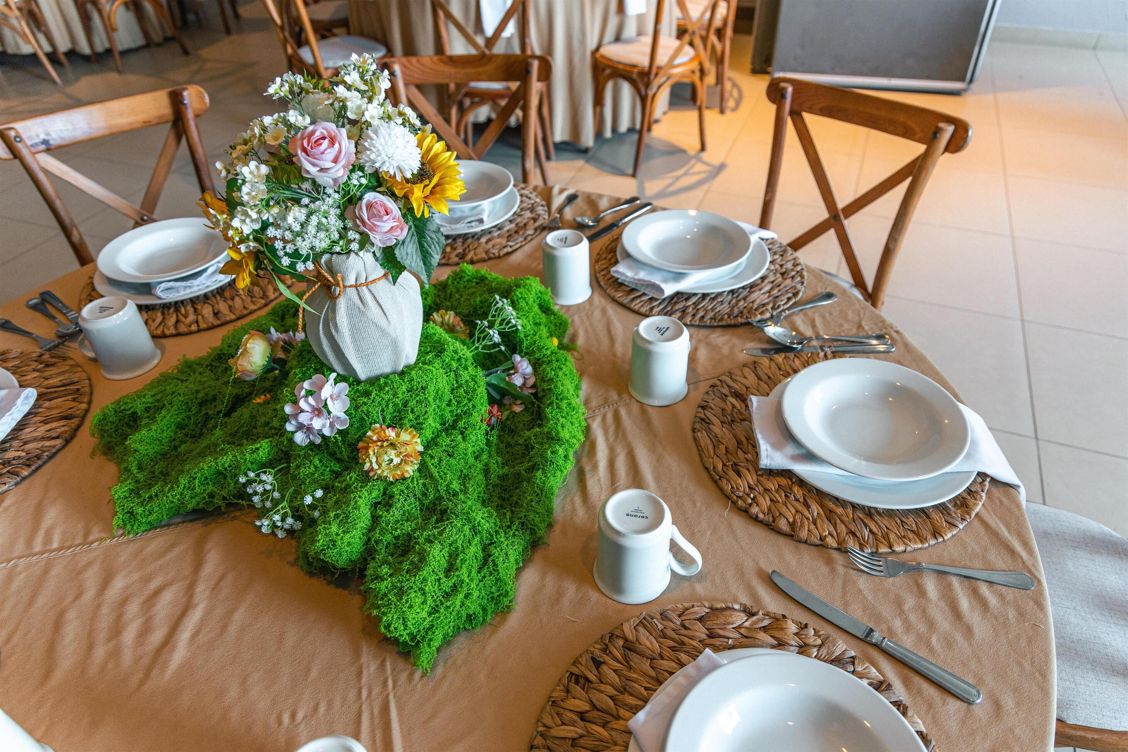 Een eettafel gedekt met borden, bestek en een middelpunt van groen en bloemen.