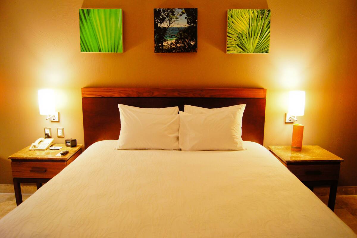 A hotel room with a large bed, two bedside tables, a nightstand, and wall-mounted artwork.