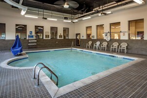 Una piscina interior con suelo de baldosas, un trampolín y varias sillas blancas a lo largo de la piscina.