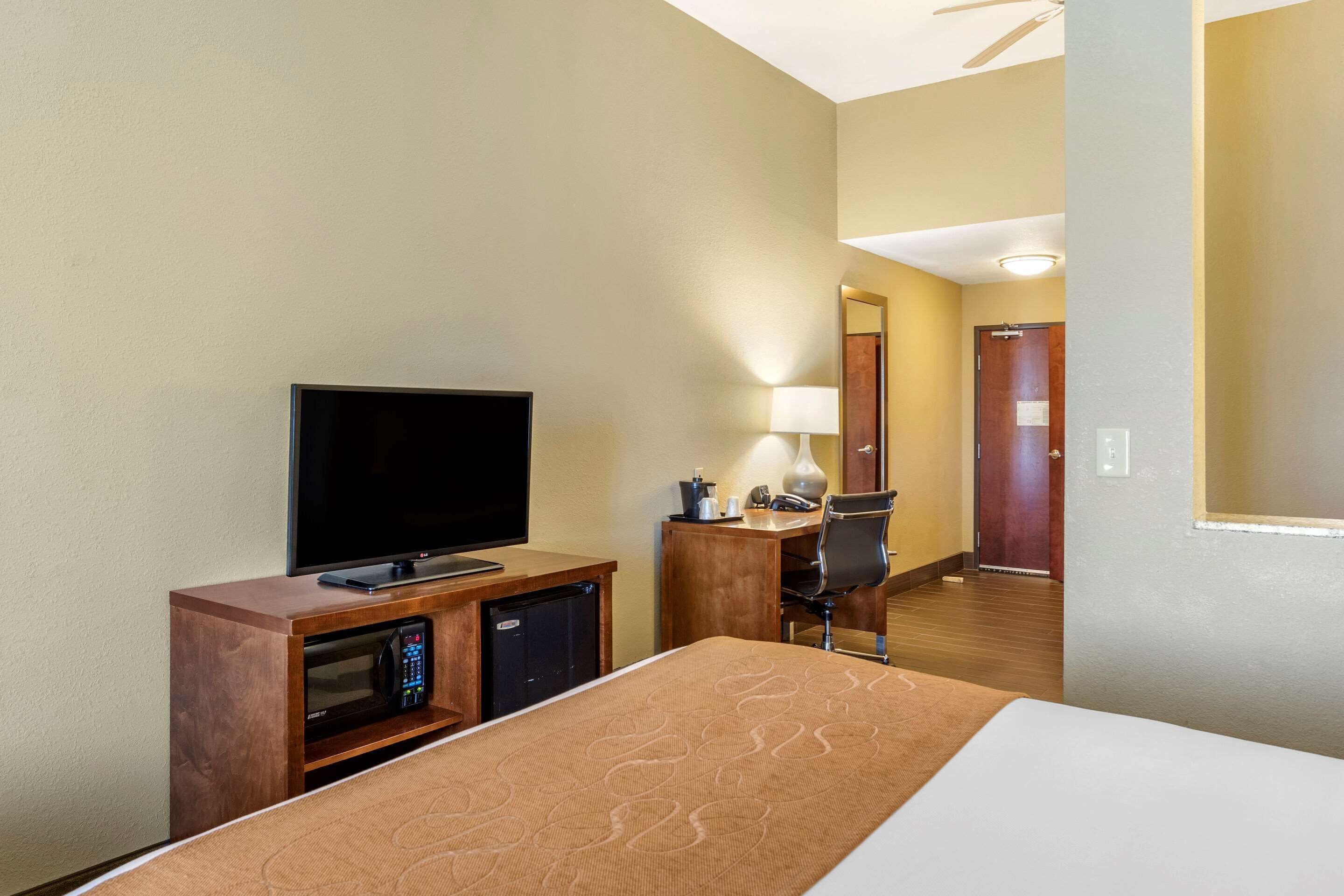 Une chambre d’hôtel équipée d’un lit, d’une télévision, d’un bureau, d’une chaise, d’une lampe et d’un four à micro-ondes.