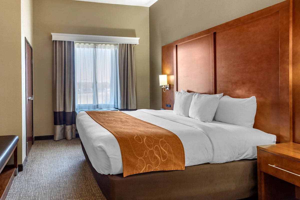 A hotel room with a large bed, a wooden headboard, a bedside table, a lamp, and a window with curtains.
