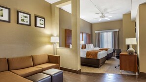 A hotel room with a sofa, a bed, a desk, and a ceiling fan. - Comfort Suites Batesville (Batesville)
