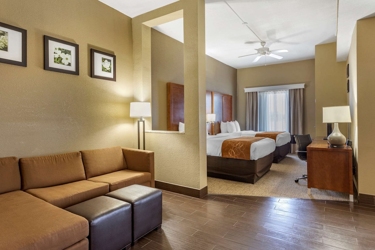 A hotel room with a sofa, a bed, a desk, and a ceiling fan.