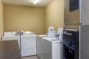 Uma área de lavanderia com quatro máquinas de lavar e secadoras Whirlpool, um dispensador de gelo e uma bancada.