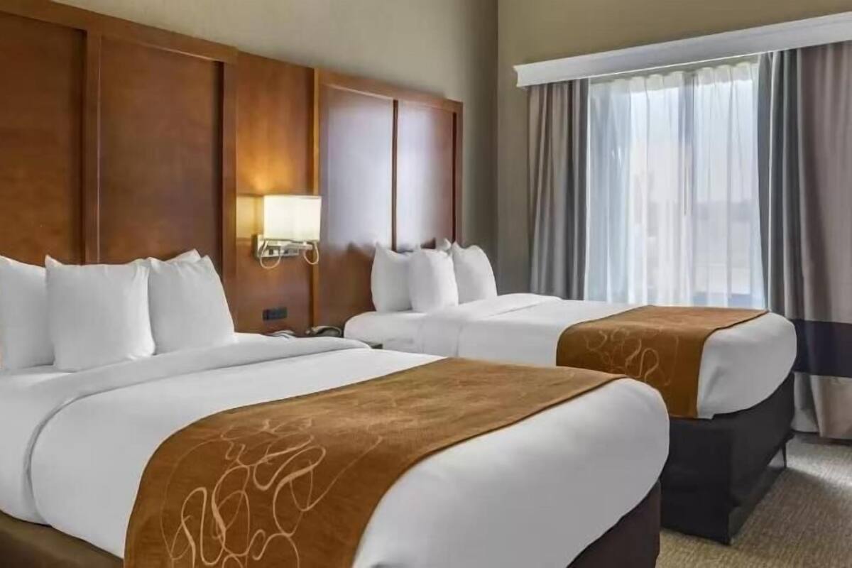 A hotel room with two beds, a wooden headboard, a nightstand, and a window with curtains.