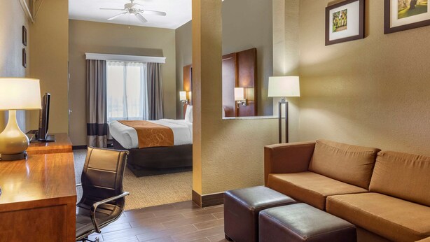 A hotel room with a bed, a desk with a lamp, a chair, a sofa, and a ceiling fan. - Comfort Suites Batesville (Batesville)