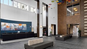 A spacious lobby with a reception desk, seating area, and a large abstract painting. - Embassy Suites Newark Airport (Elizabeth)