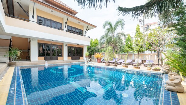 A swimming pool with a tiled deck, surrounded by lounge chairs and potted plants. - Chaba Garden Resort & Service (Pattaya)