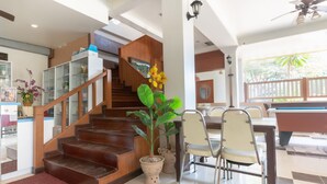 A spacious indoor area with a wooden staircase, a dining table with chairs, and a pool table. - Chaba Garden Resort & Service (Pattaya)