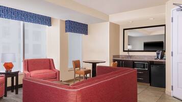 Een hotelkamer met kitchenette, een eethoek met tafel en stoelen, een bank en een grote spiegel.