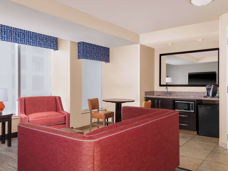 Een hotelkamer met kitchenette, een eethoek met tafel en stoelen, een bank en een grote spiegel.