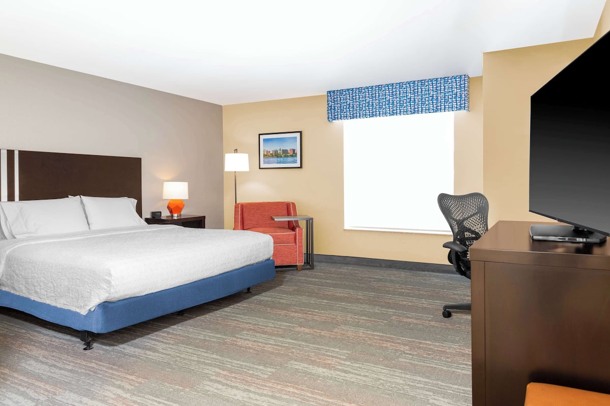 Habitación de hotel con cama, escritorio, silla, lámpara, un cuadro en la pared y ventana.