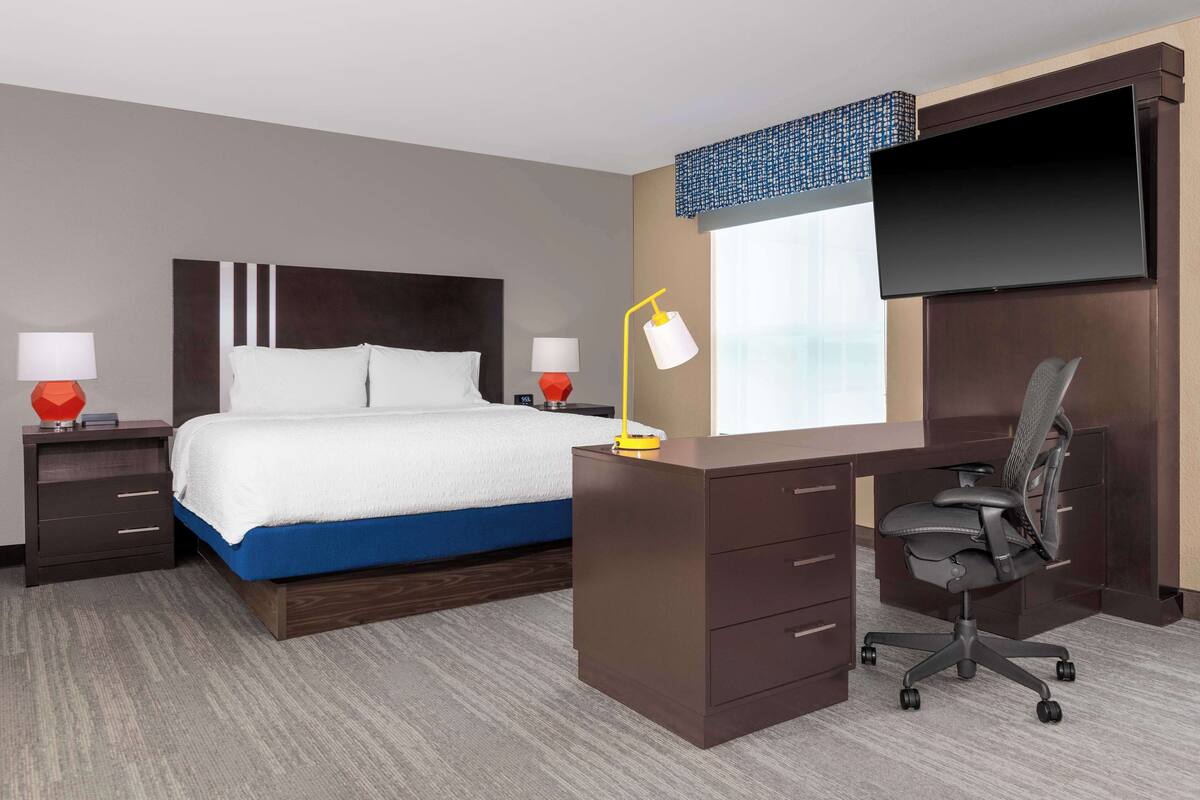 Una habitación de hotel con una cama, un escritorio con una silla, un televisor y dos lámparas.