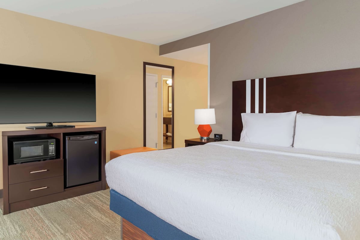 Una habitación de hotel con una cama grande, un televisor de pantalla plana, un microondas y un refrigerador en un mueble de madera.