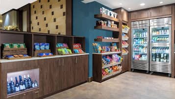 A snack bar with shelves stocked with various snacks and beverages, a refrigerated display case, and a wooden wall with a grid pattern.
