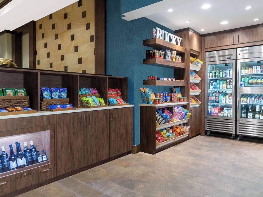 A snack bar with shelves stocked with various snacks and beverages, a refrigerated display case, and a wooden wall with a grid pattern.