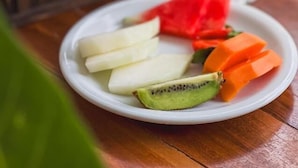 A plate of sliced fruits including kiwi, watermelon, and apple, and a glass of orange juice on a wooden table. -  Pousada Porto Verano (Ipojuca)