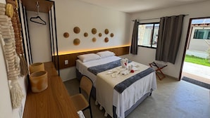 A hotel room with two beds, a wooden desk, a hanging coat rack, and a view of the outside. -  Pousada Porto Verano (Ipojuca)