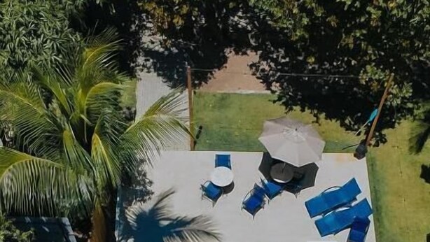 An aerial view of a rectangular swimming pool with two people in the water, surrounded by lounge chairs and umbrellas. -  Pousada Porto Verano (Ipojuca)