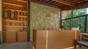 Una recepción con un fondo de pared de piedra, estanterías de madera con objetos decorativos y un banco.