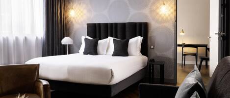 Une chambre d’hôtel dotée d’un grand lit, d’un coin salon avec un canapé et un fauteuil, d’une petite table et d’un bureau avec une chaise.