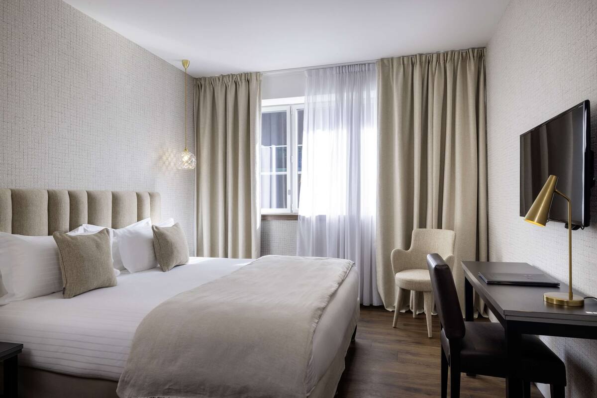 Een hotelkamer met een groot bed, een bureau met een laptop, een stoel en een televisie aan de muur.
