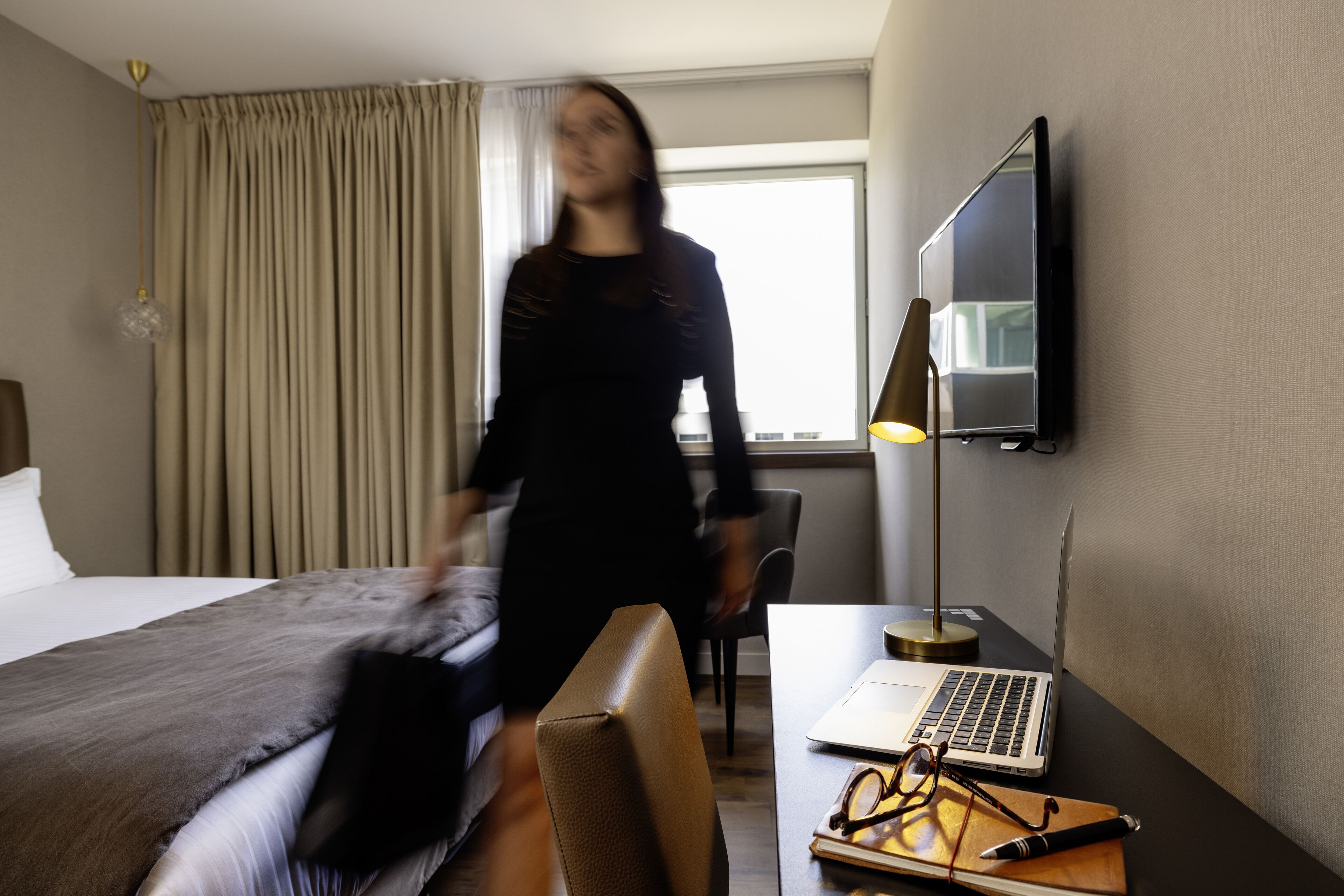 Una habitación de hotel con una cama, un escritorio con una computadora portátil, una silla y un televisor en la pared.