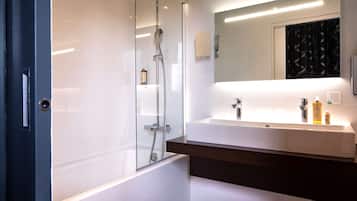 A modern bathroom with a glass-enclosed shower, a white sink with a wooden countertop, and a large mirror above the sink.