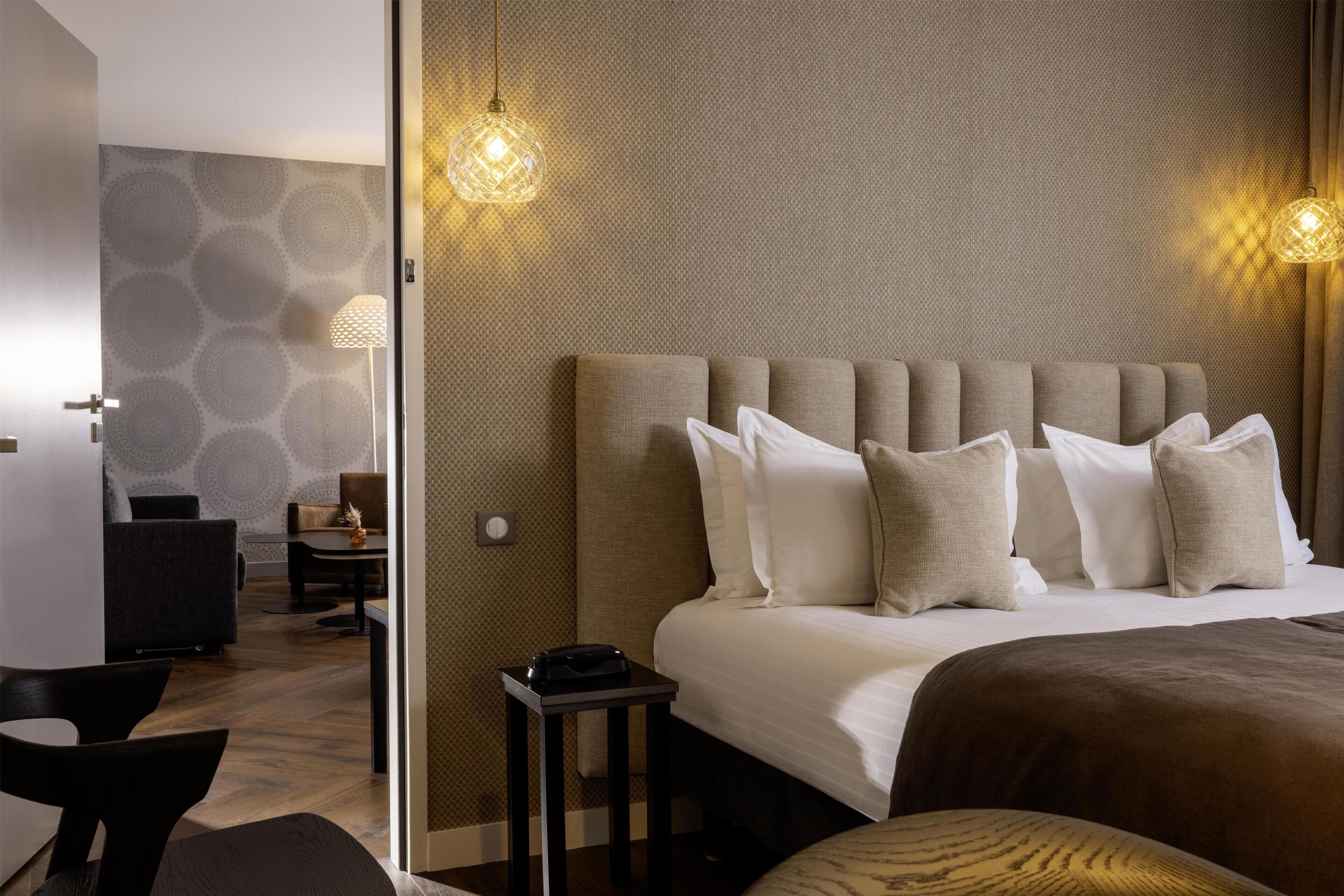 A hotel room with a large bed, a bedside table, a lamp, and a wall with a geometric pattern.