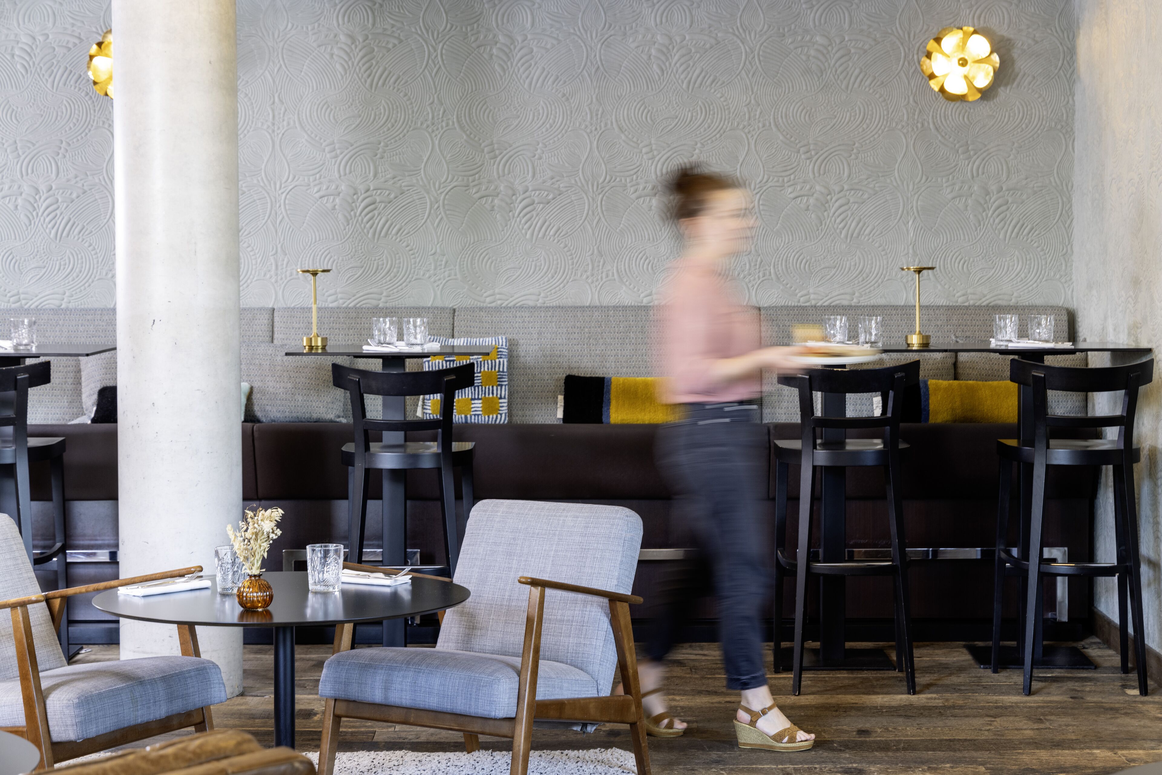 A restaurant interior with round tables, cushioned seating, and decorative lighting.