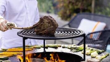 A chef grilling meat on an outdoor grill with vegetables.