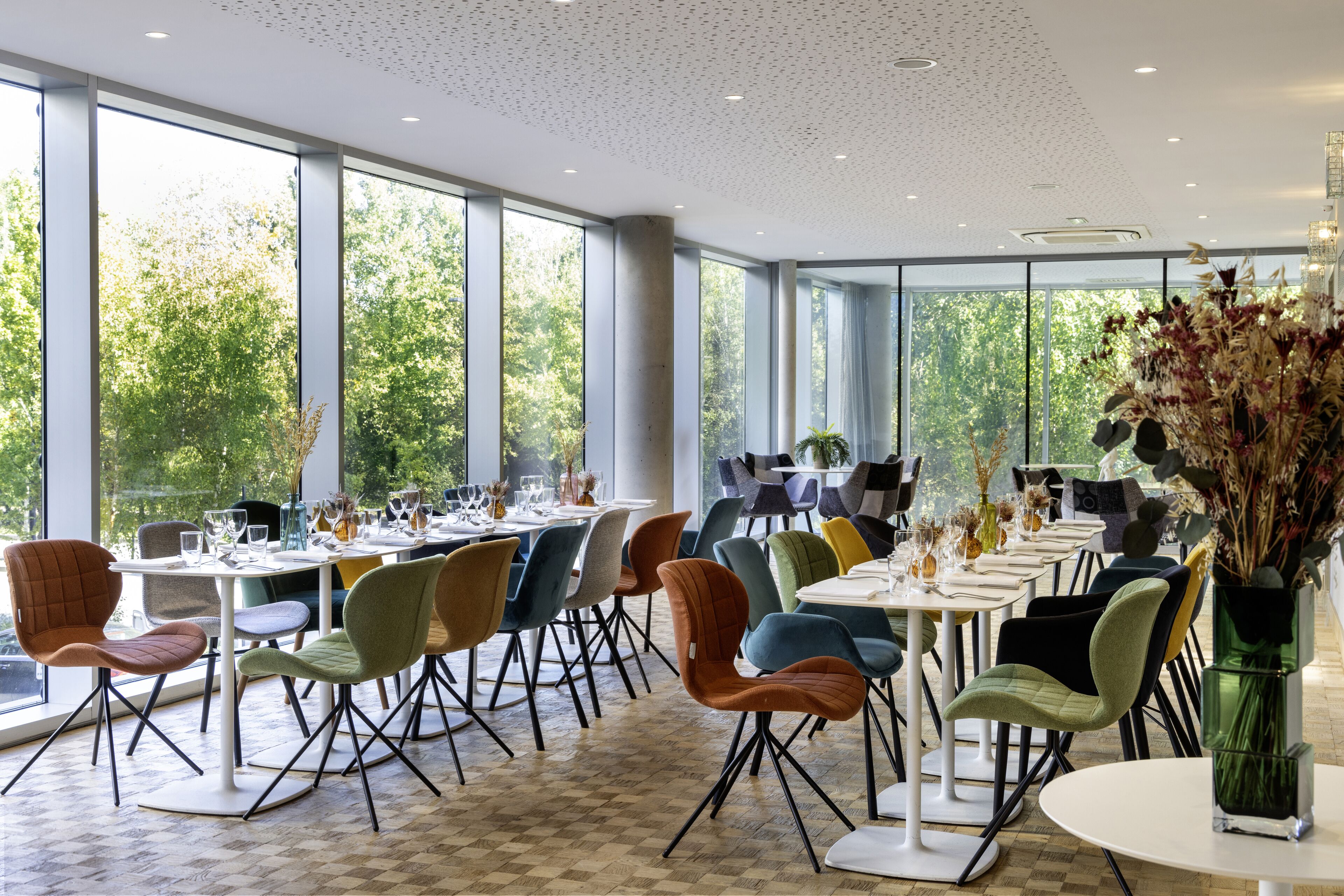 A spacious dining area with large windows, modern chairs, and tables set for dining.