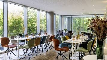 A spacious dining area with large windows, modern chairs, and tables set for dining.