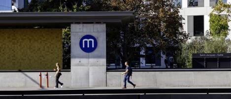 Un edificio moderno con un llamativo logotipo 'm', una pasarela peatonal y un letrero que dice 'Saint-Jacques - Gaieté'.