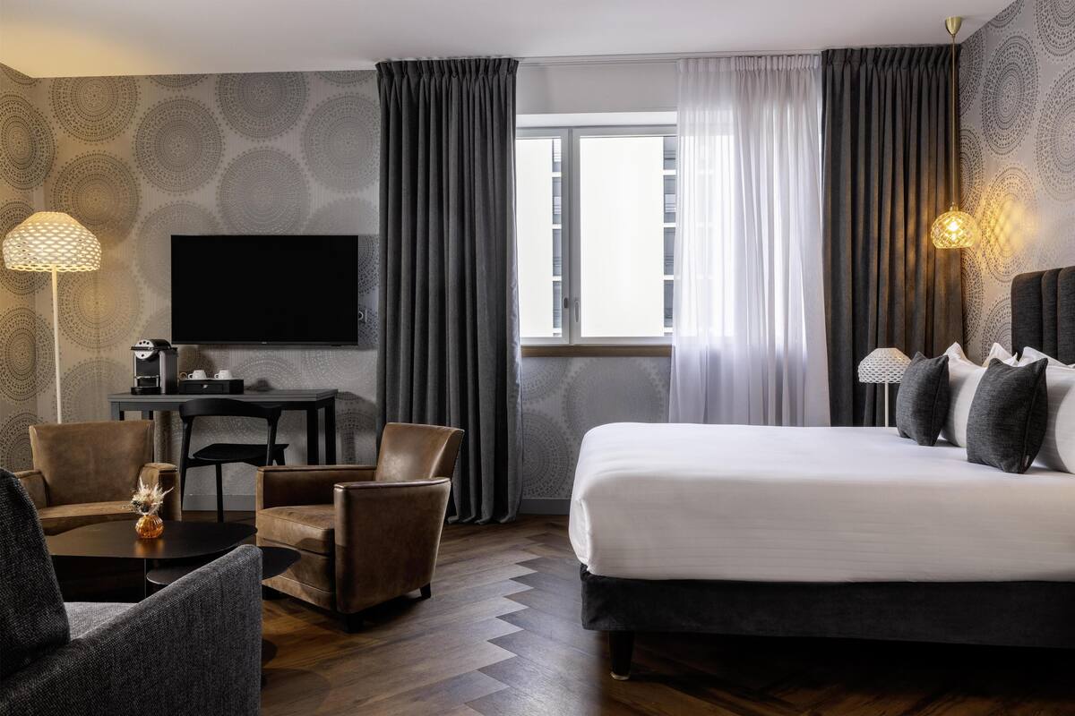 Een hotelkamer met een bed, twee fauteuils, een tafeltje, een televisie en een raam met gordijnen.