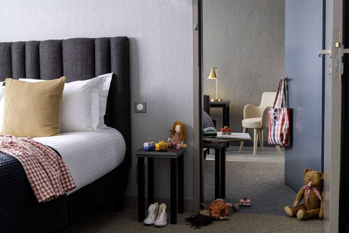 Een hotelkamer met een bed, een tafeltje, een stoel en een knuffelbeer.