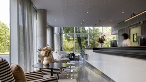 Een moderne hotellobby met een receptiebalie, een zithoek met gestreepte banken en grote ramen met uitzicht op het omliggende landschap.