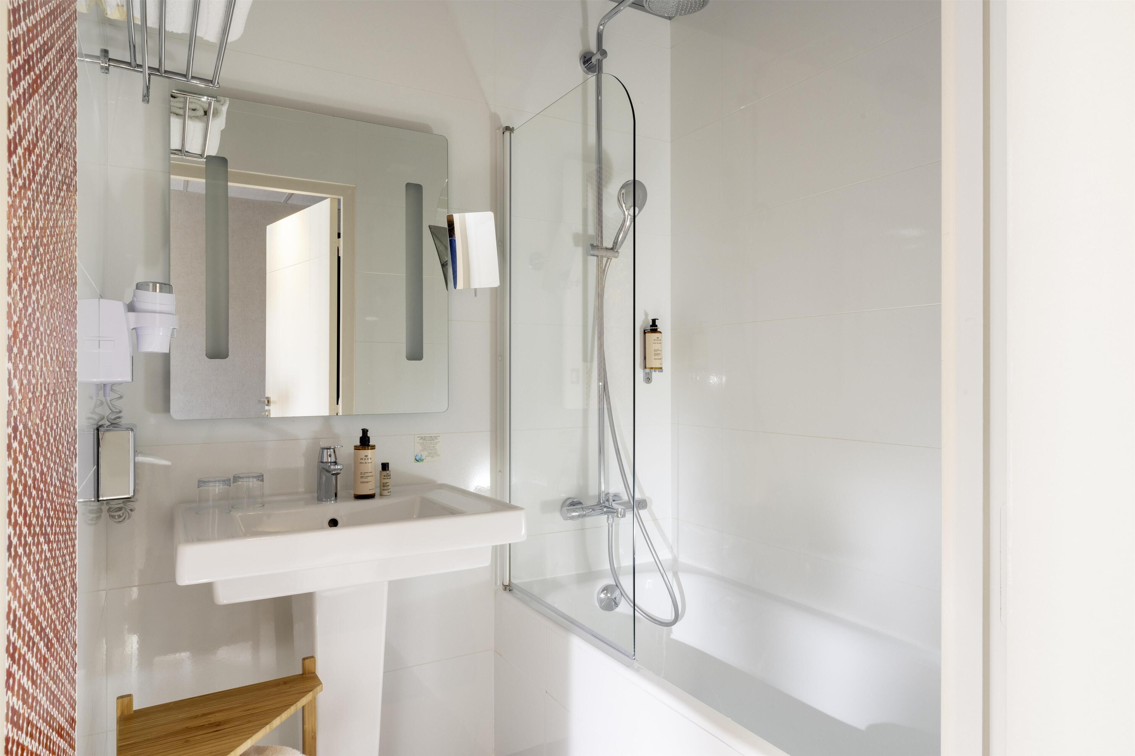 A modern bathroom with a white sink, mirror, and glass-enclosed shower.