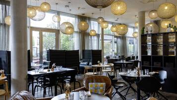 Interior de restaurante con lámparas de fibra redondas, ventanas amplias y diferentes tipos de mesasillas.
