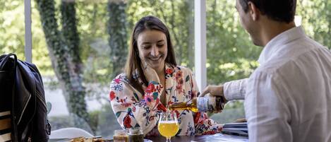Una persona sirviendo una bebida en un vaso sobre una mesa con una computadora portátil, una bolsa y una bandeja con comida.
