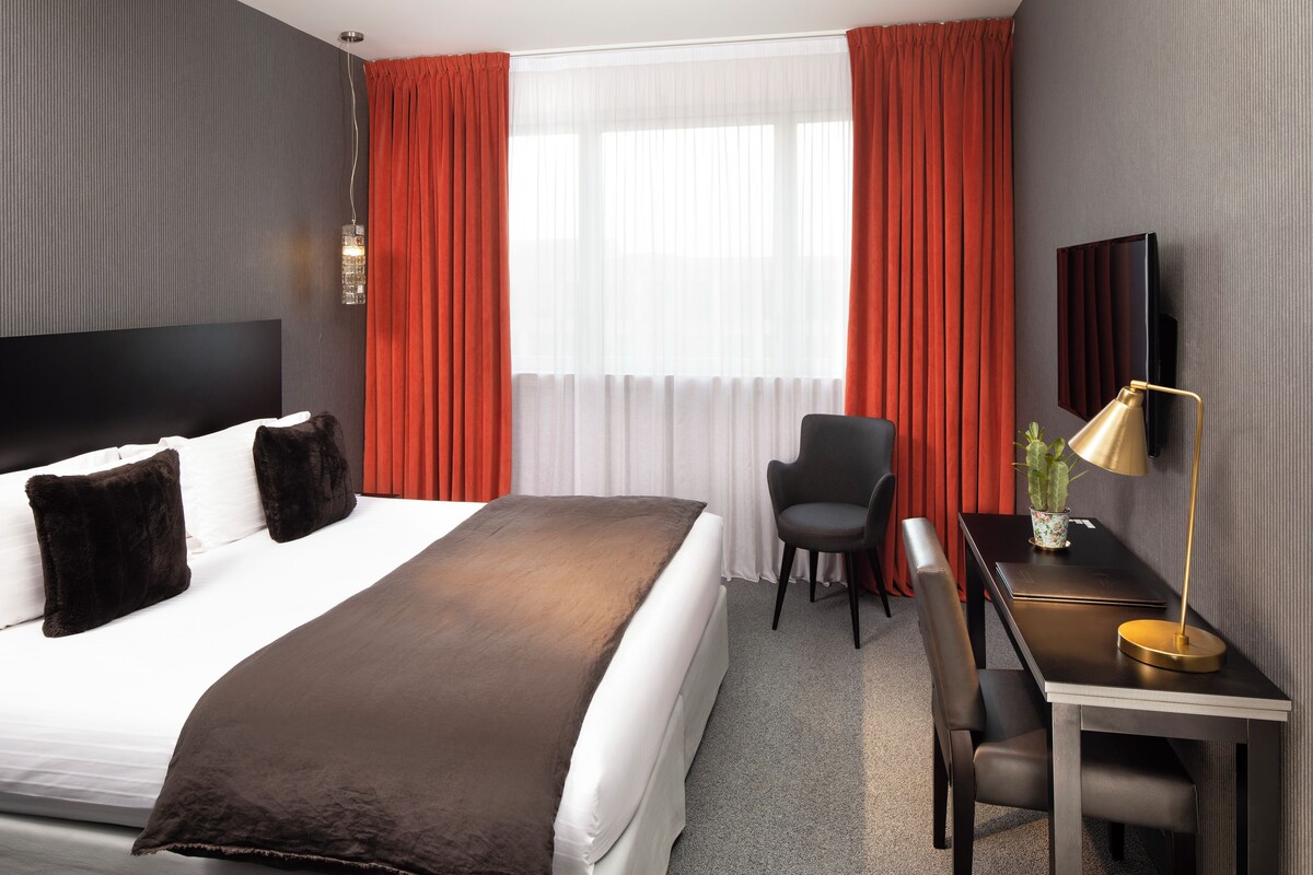 Een hotelkamer met een bed, bureau, stoel, televisie en raam met gordijnen.