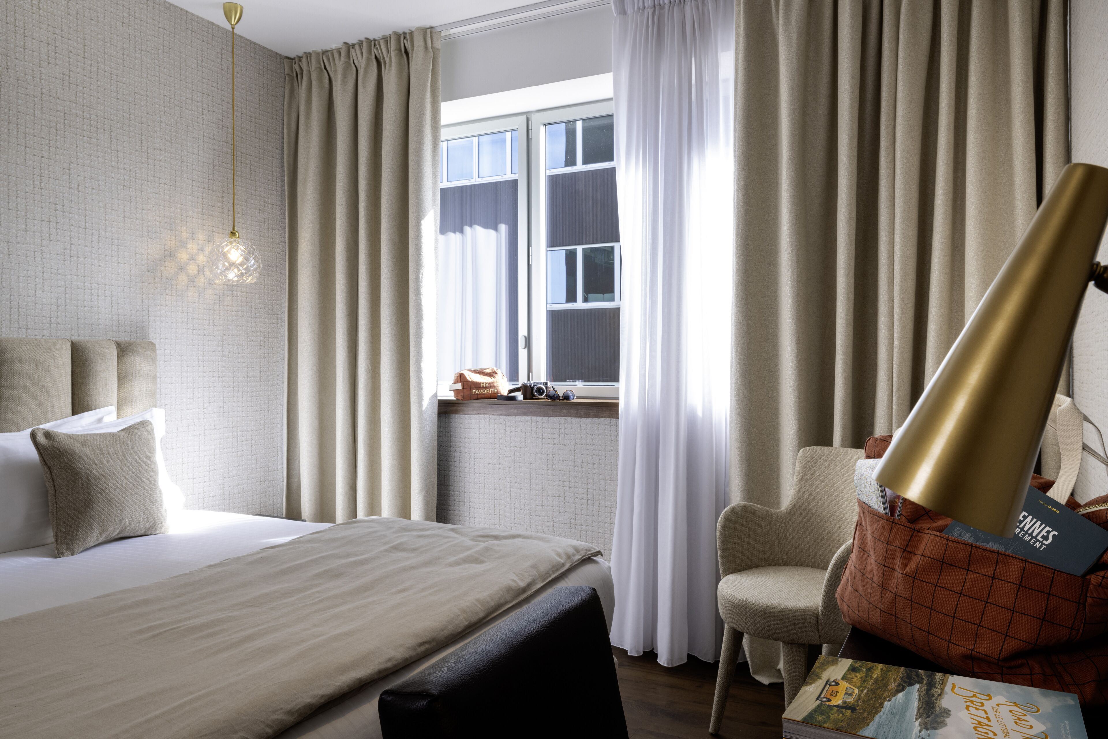 Una habitación de hotel con una cama, una silla, un escritorio con lámpara y una ventana con cortinas.