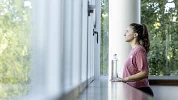 A person standing by a window with a view of trees, holding a water bottle.