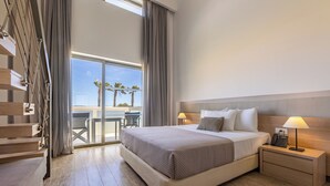 A modern hotel room with a large bed, a nightstand with a lamp, and a view of palm trees through the window. - Akti Palace Hotel - All inclusive (Kos)